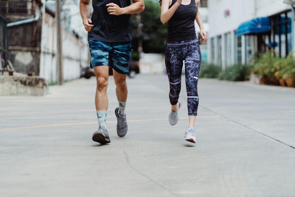 Two adults jogging in trendy activewear and sneakers on a city street, promoting fitness and healthy lifestyle.