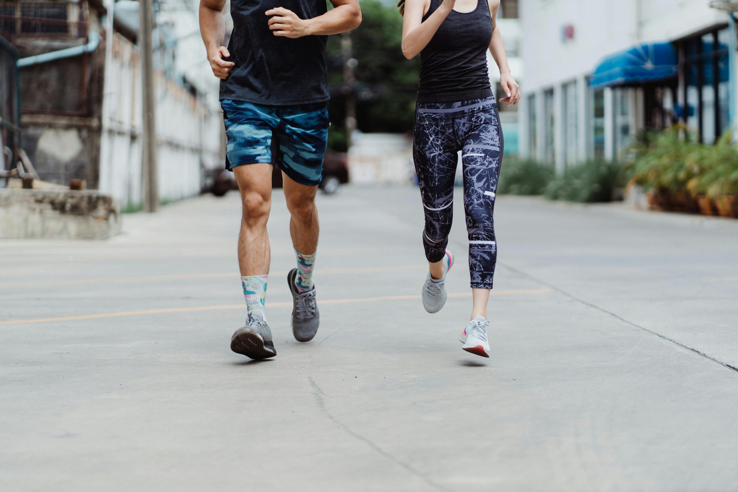 Two adults jogging in trendy activewear and sneakers on a city street, promoting fitness and healthy lifestyle.