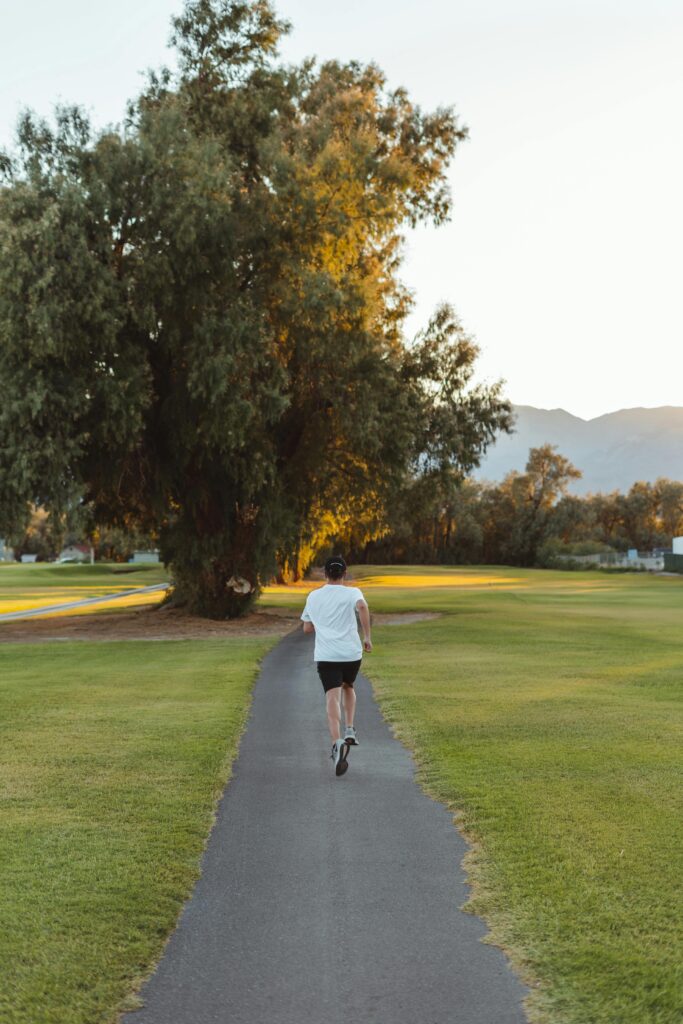 A person jogging on a serene morning path in a sunlit park surrounded by nature.